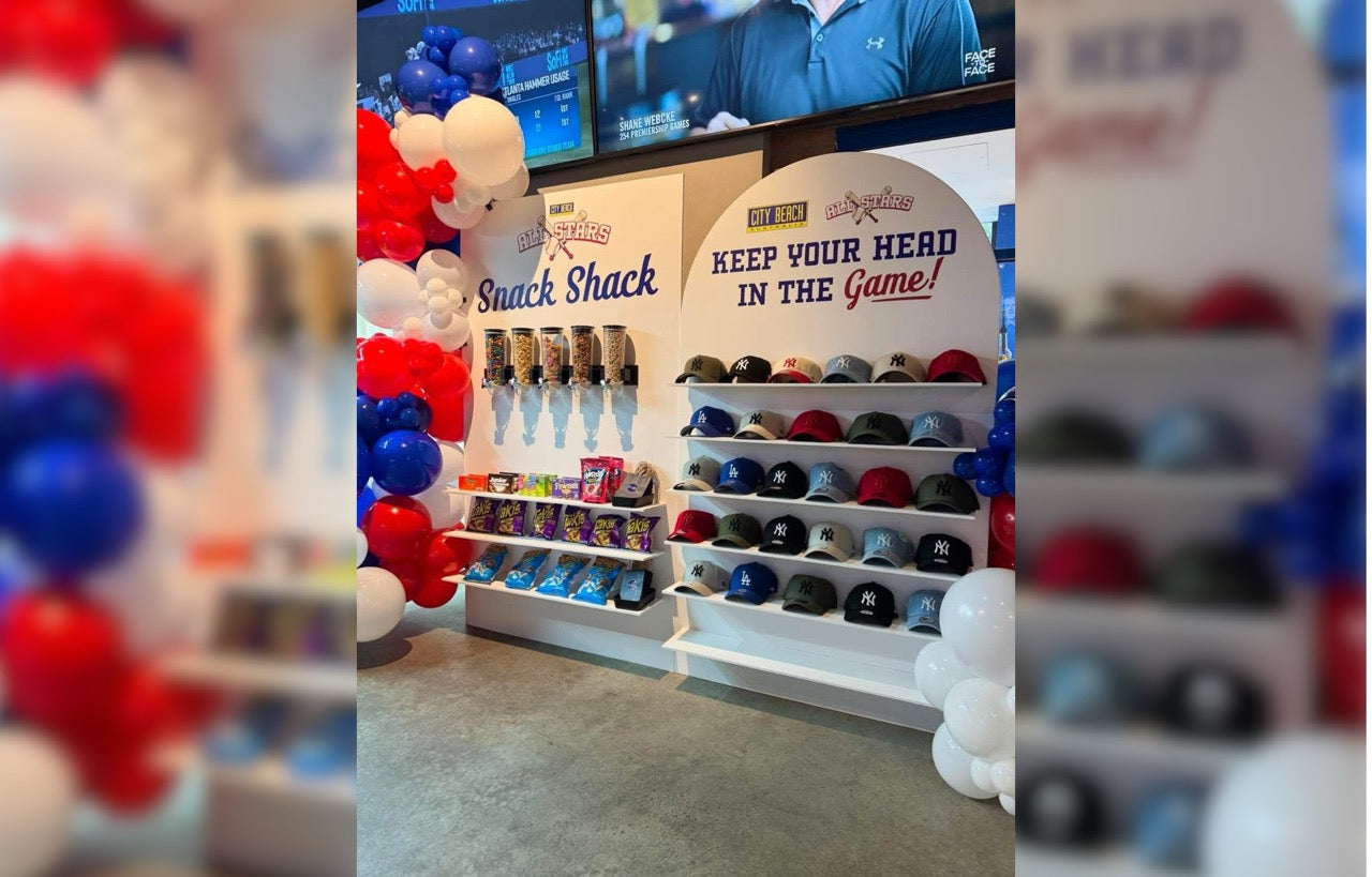 Display of sports caps and snacks with promotional signs in a store setting.