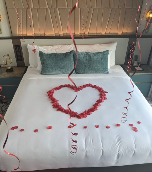 Decorative heart made of rose petals on a bed with green pillows and red ribbons.
