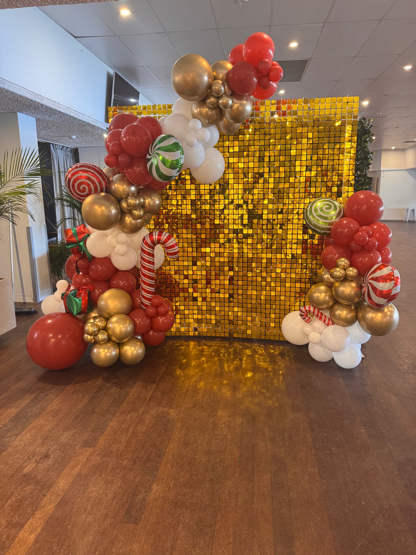 Decorative balloon arch with red, gold, and white balloons in front of a gold sequin backdrop.