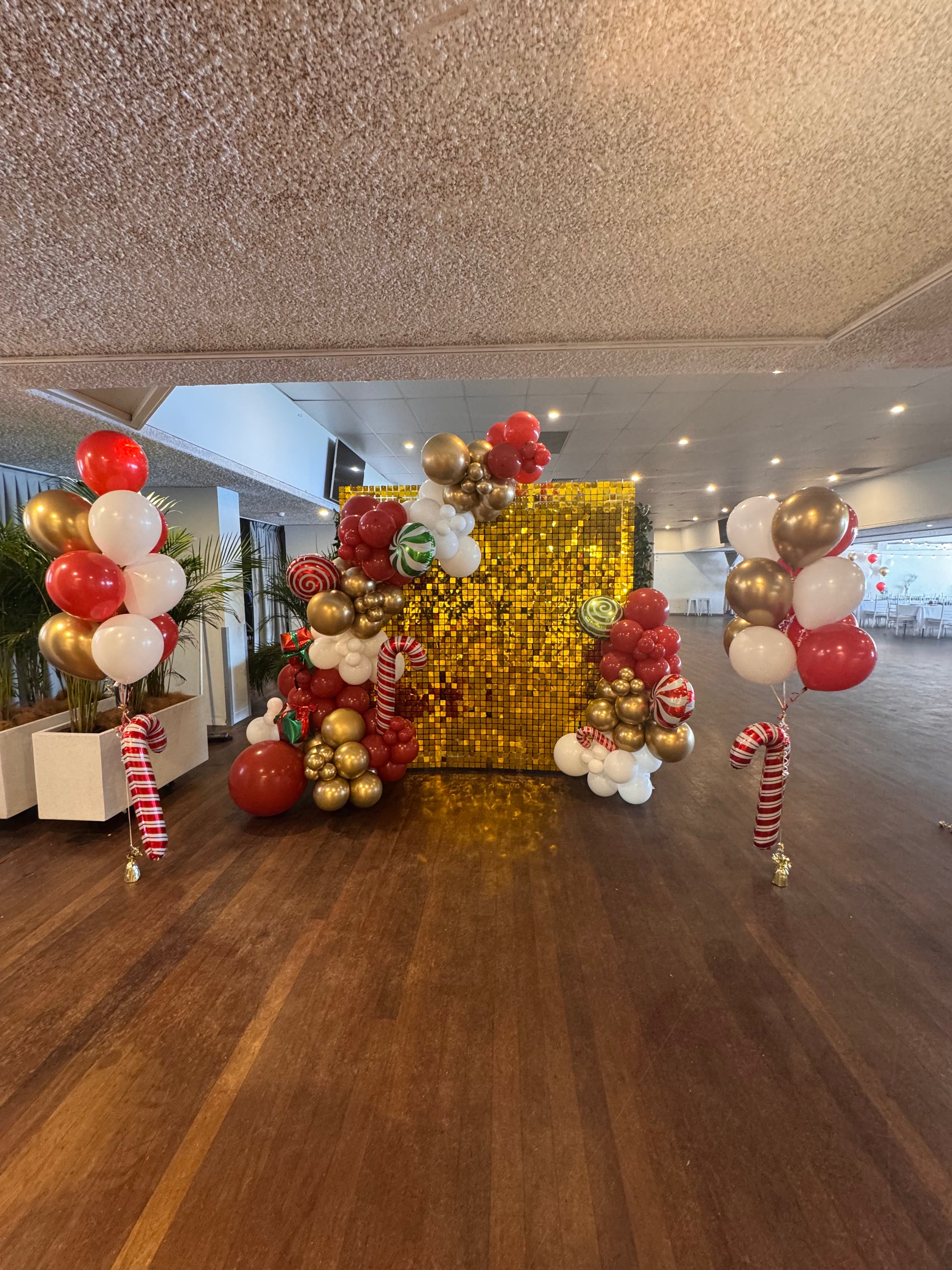 Decorative balloon arch with gold and red balloons in a room with wooden flooring.