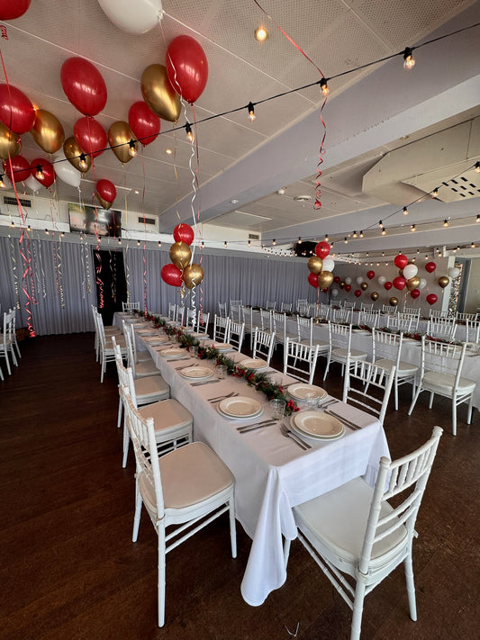 Dining hall with tables set for a meal, balloons, and string lights.