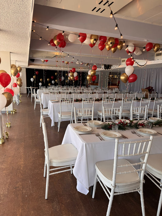 Dining hall with tables set for a meal, white chairs, and red and gold balloons.